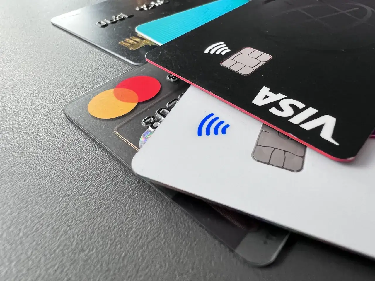 Nahaufnahme von Kreditkarten, darunter eine schwarze Karte mit dem **VISA**-Logo und eine transparente Karte mit dem Mastercard-Logo.