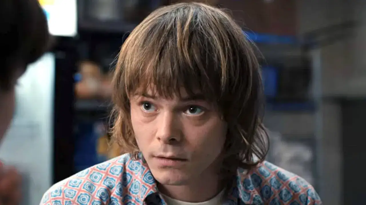 Charlie Heaton w koszuli w geometryczne wzory, z charakterystyczną fryzurą, patrzy w bok z zamyśloną miną.