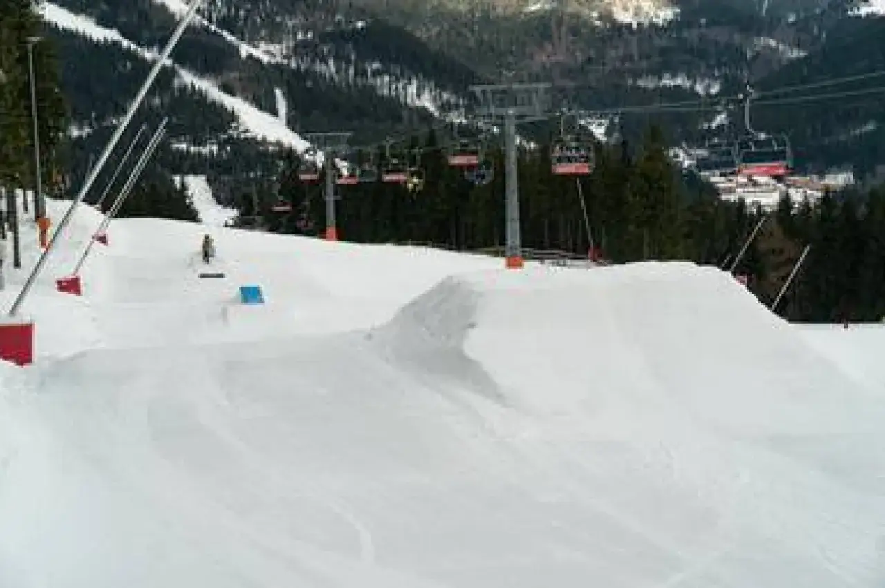 Spindleruv Mlyn snowpark: śnieżne muldy i skocznia czekają na snowboardzistów. W tle kolejka linowa.
