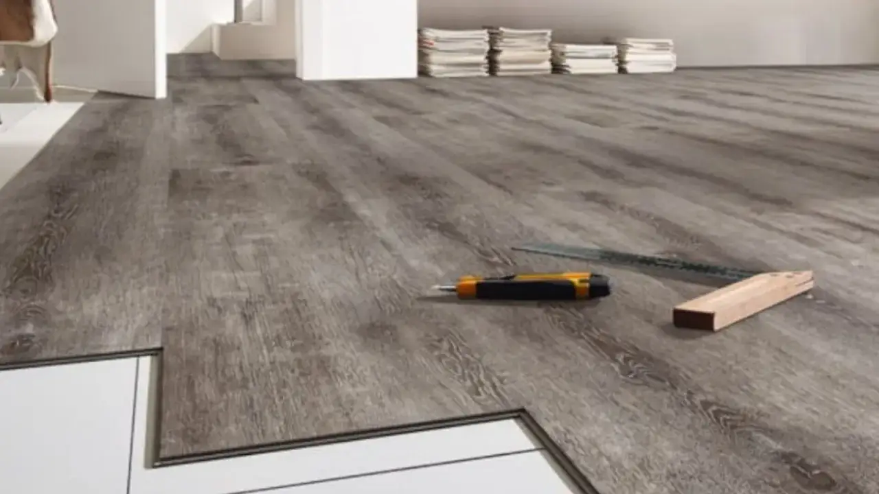 Installazione pavimento LVT: pro e contro. Taglierino e squadra pronti per il lavoro su un moderno pavimento effetto legno grigio.