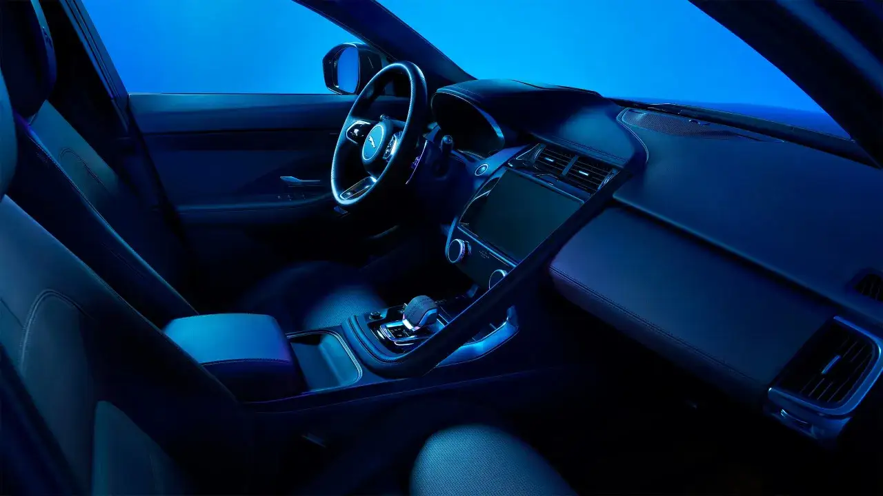 Interior del Jaguar E-Pace con iluminaci&oacute;n ambiental azul. El volante, la consola central y la pantalla t&aacute;ctil son visibles. Las opiniones sobre el Jaguar E-Pace destacan su dise&ntilde;o.