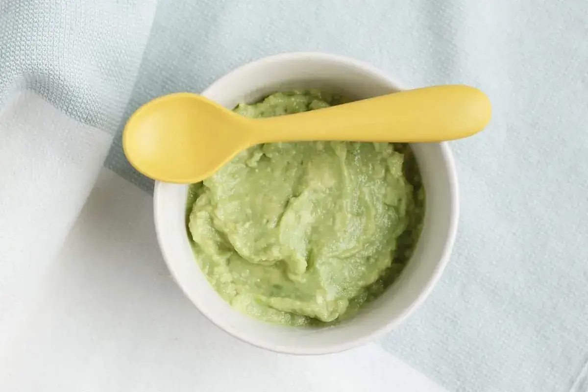 Papilla de aguacate beb&eacute; 6 meses en un cuenco blanco con cuchara amarilla.