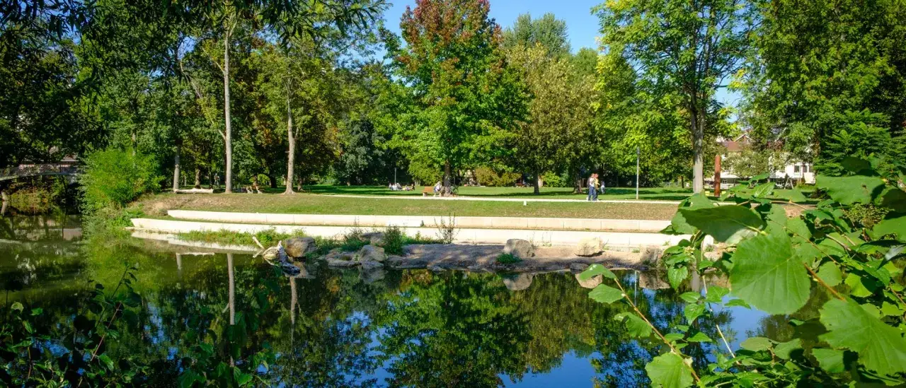 Idyllischer Park mit Teich und Bäumen, Menschen genießen die Sonne im Talaue Waiblingen.