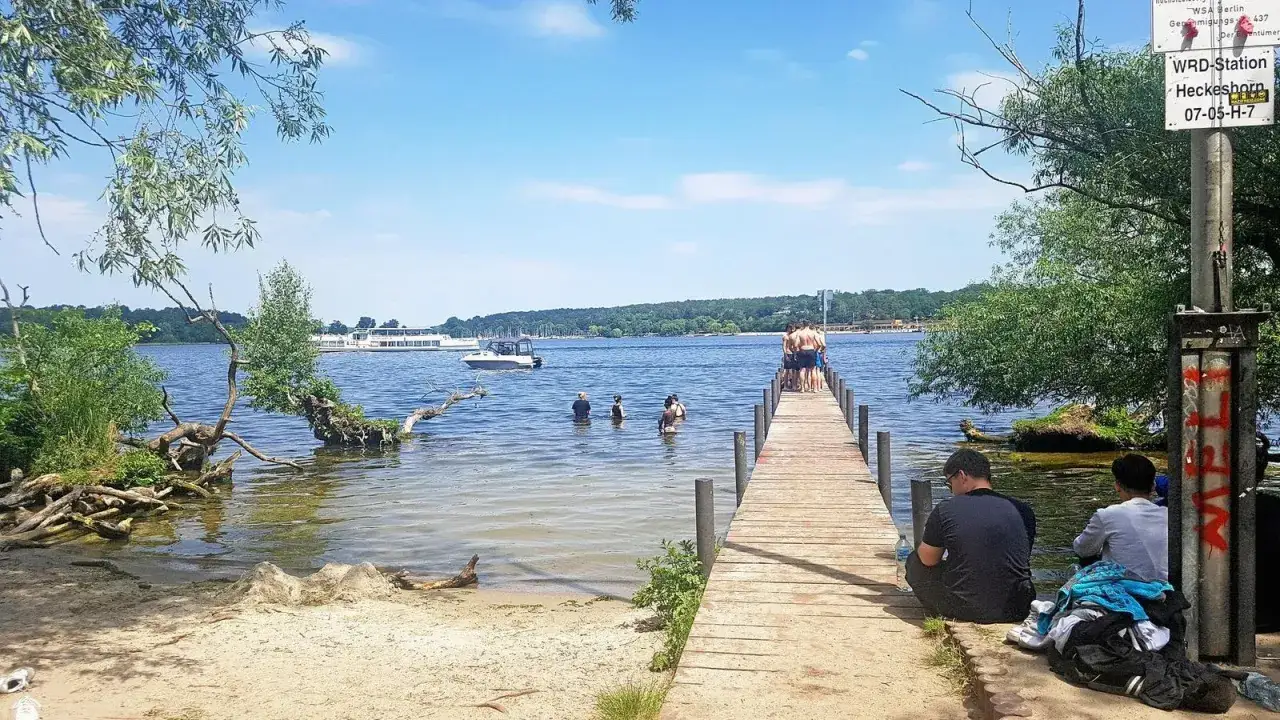 Sommer am Wannsee Berlin: Menschen planschen im Wasser, andere sitzen am Steg. Ein Schiff f&auml;hrt vorbei.