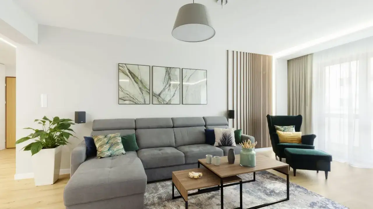 Nowoczesny salon: szara sofa, zielony fotel, drewniane panele i obrazy. Inspiracja, jak urządzić salon.