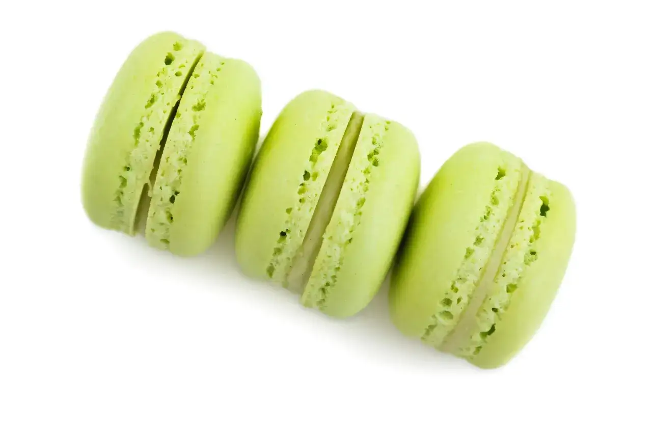 Trois macarons verts vifs, garniture &agrave; la ganache pistache, sur fond blanc.