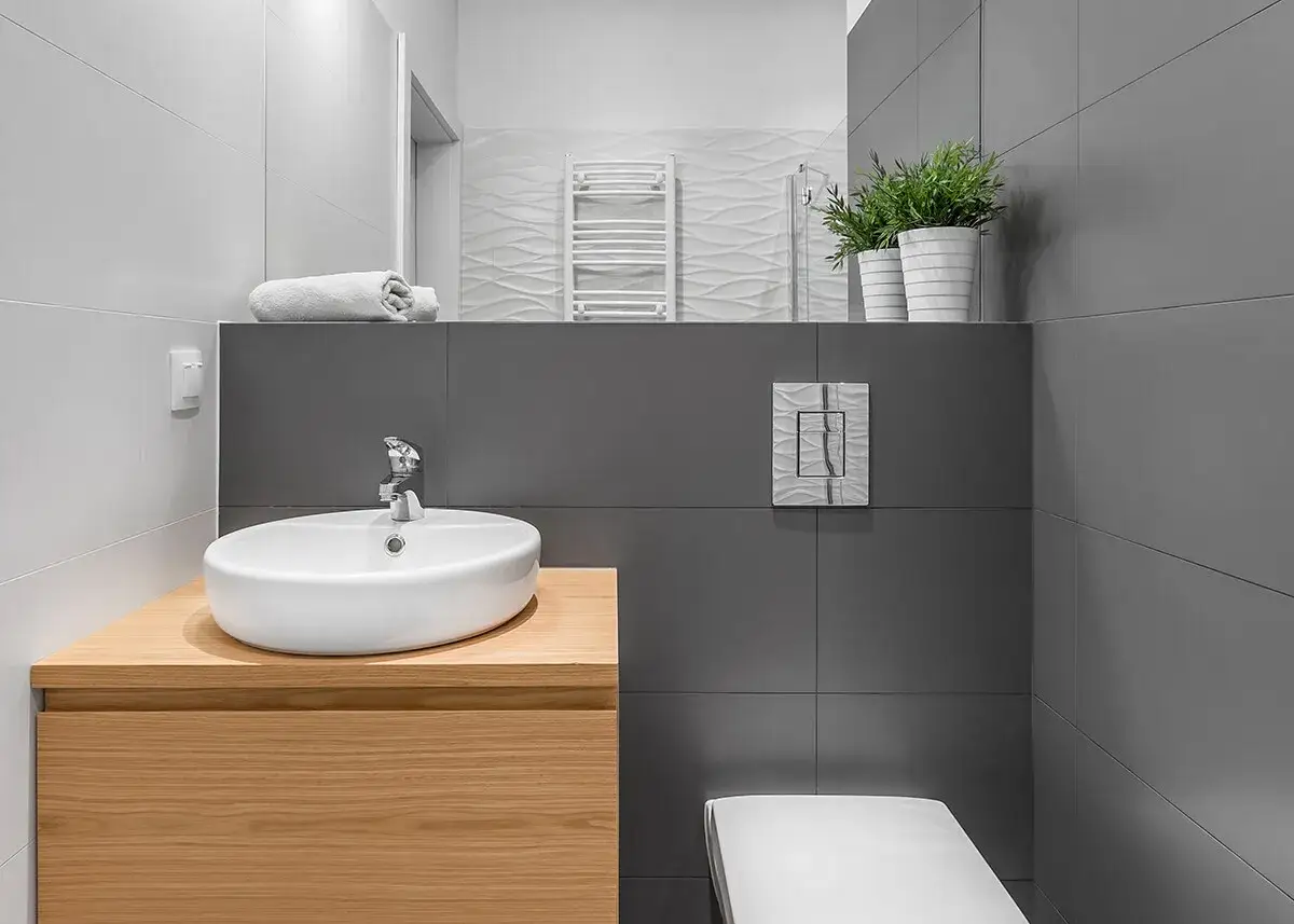 Baño moderno con lavabo sobre mueble de madera. Ideas para como sacar la humedad del baño sin ventilación: plantas y toallas enrolladas.