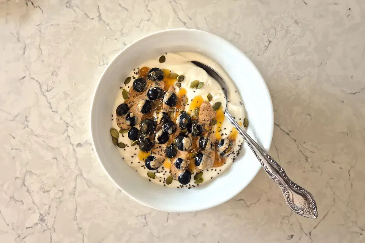 Una ciotola di yogurt greco con mirtilli, semi di chia, semi di zucca e burro di mandorle. Una colazione proteica dolce e salutare.