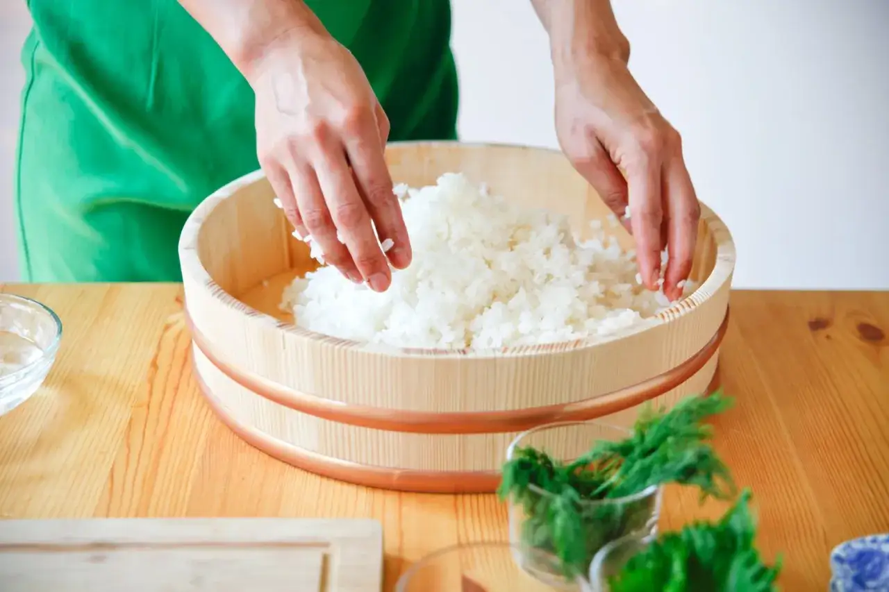 Dłonie mieszają ryż w drewnianym naczyniu, przygotowując go do sushi. Klucz do sukcesu: jak ugotować ryż do sushi.