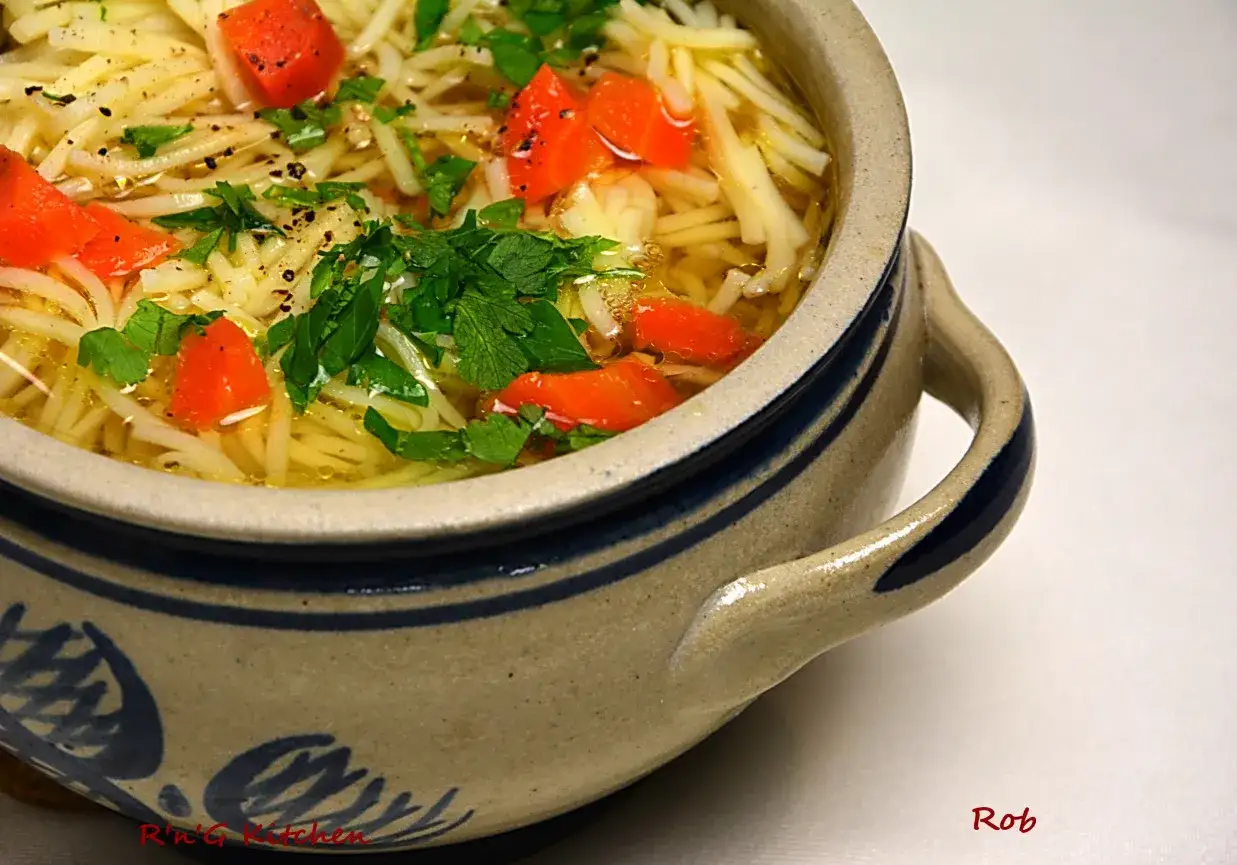 Aromaticzny rosół z perliczki z makaronem i kawałkami marchewki, udekorowany świeżą natką pietruszki.