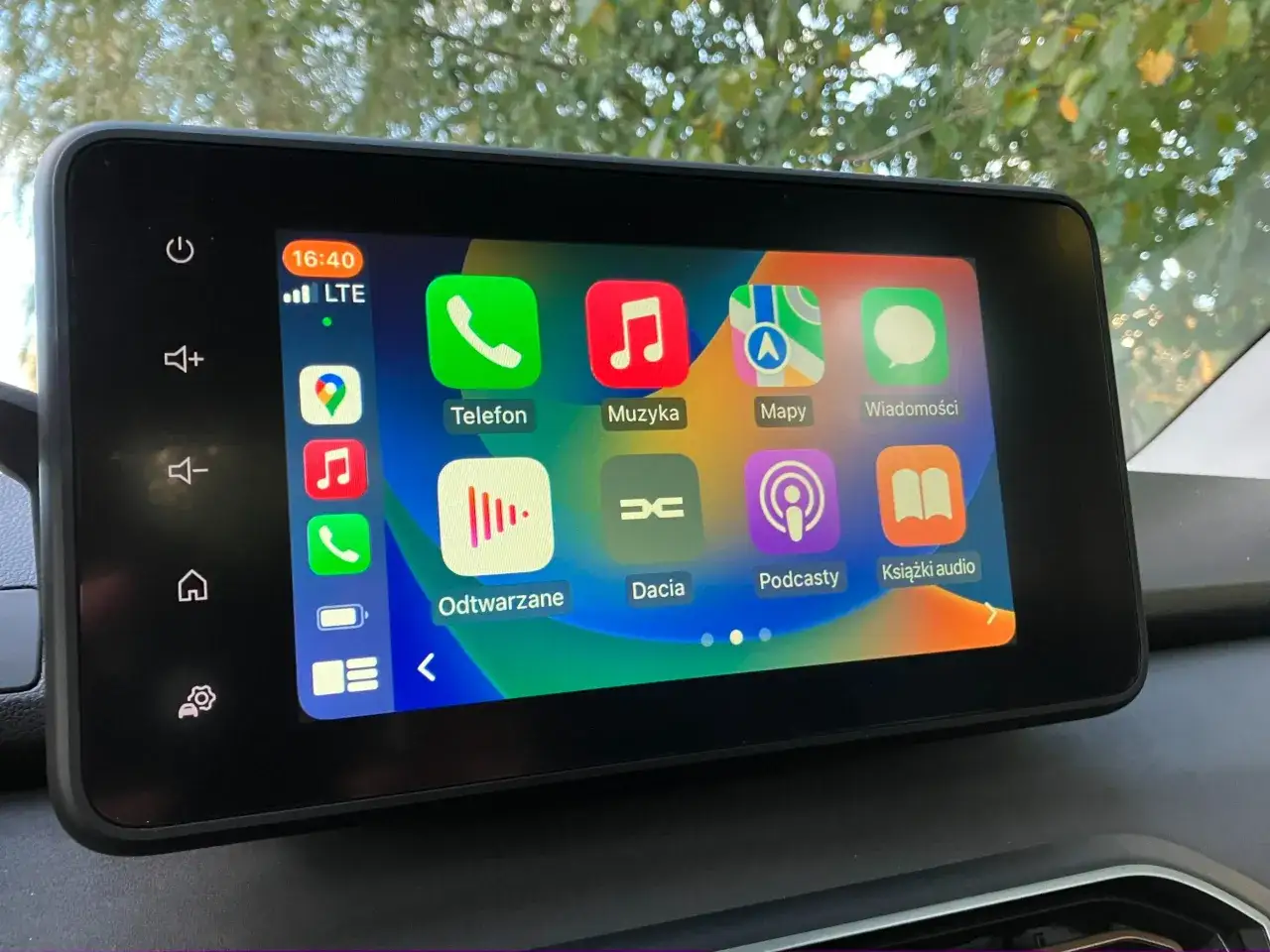 Ekran multimedialny w samochodzie z ikonami: Telefon, Muzyka, Mapy, Wiadomości, Dacia, Podcasty, Książki audio. Może to być alternatywa dla tradycyjnego podatku od radia w samochodzie.