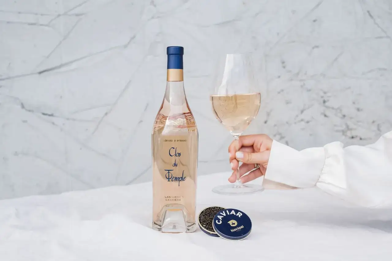 Une main tient un verre de rosé. À côté, une bouteille et une boîte de caviar. Le temps de conservation d'un rosé ouvert est court, mais ce moment est parfait.