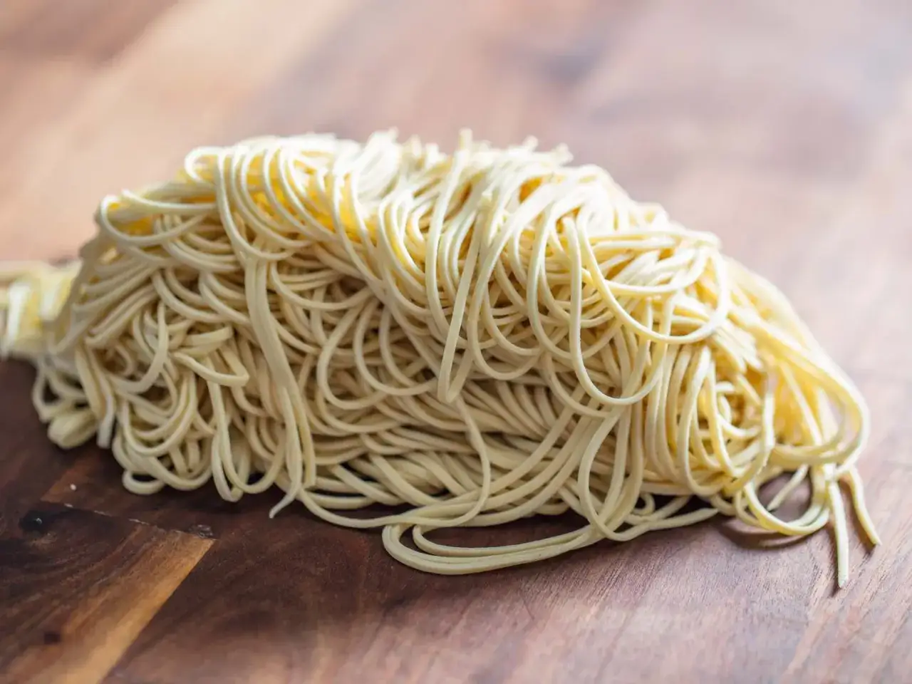 Stos świeżego, żółtego makaronu alkalicznego ułożony na drewnianej desce. Idealny do ramen.