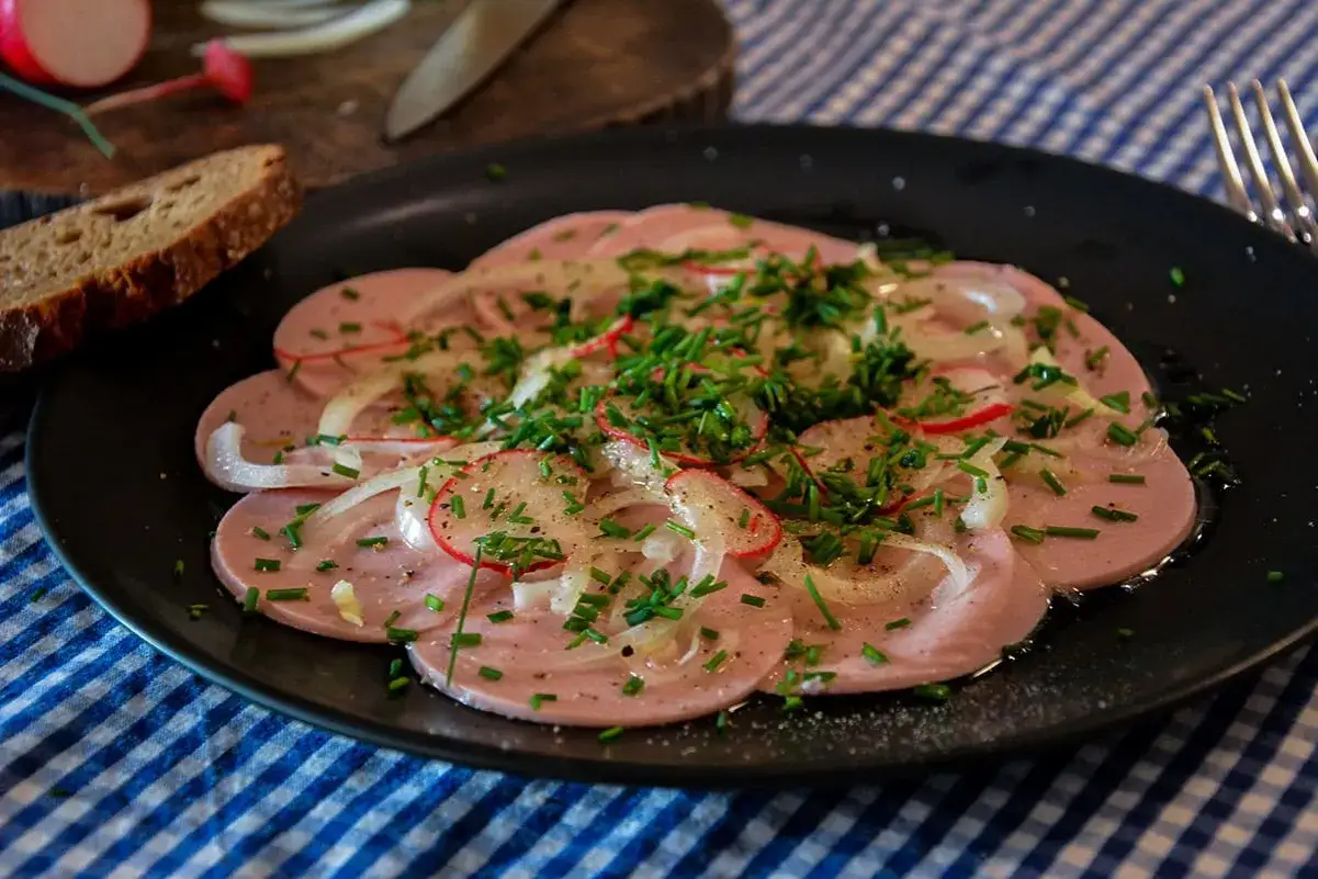 Saure Wurst mit Zwiebeln, Radieschen und Schnittlauch bestreut, serviert mit Brot.
