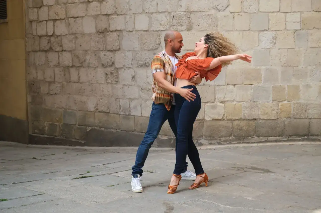 Coppia balla salsa e bachata per strada, con un uomo che guida e una donna che si abbandona al movimento.