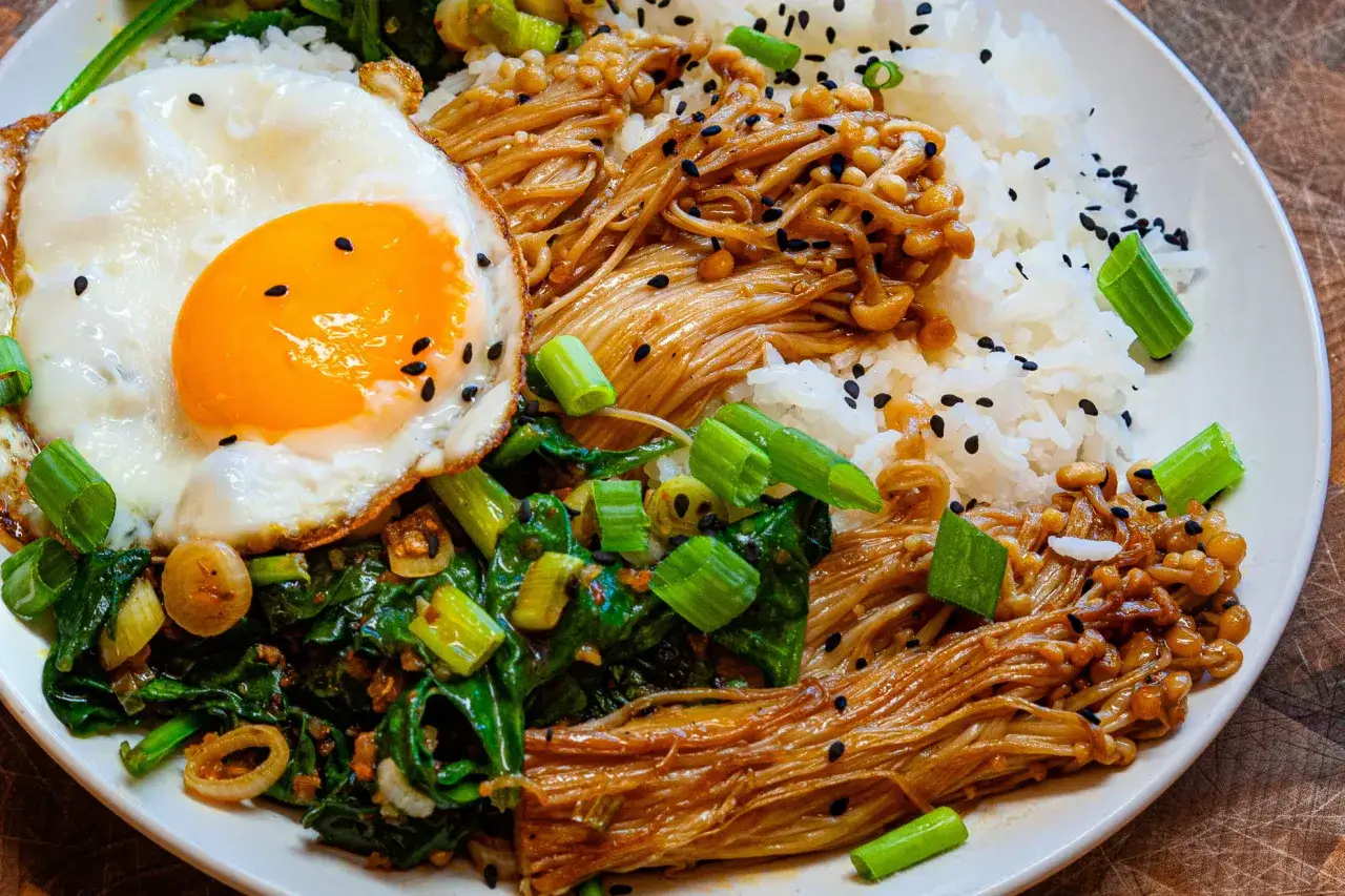 Rezept für Enoki Pilze: Reis mit gebratenen Enoki Pilzen, Spinat und Spiegelei, garniert mit Frühlingszwiebeln und schwarzem Sesam.