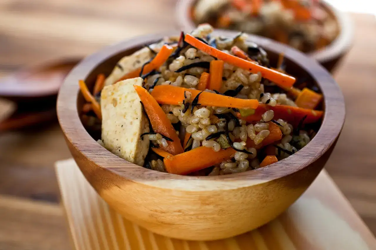 Un bol en bois rempli de riz germ&eacute;, de carottes coup&eacute;es en julienne et de tofu.