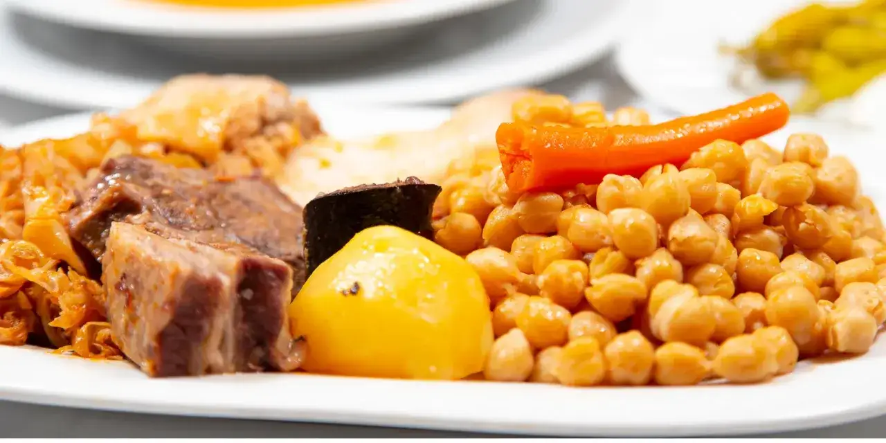 Un plato abundante con garbanzos, carne, repollo y zanahoria, perfecto para una taberna y media.