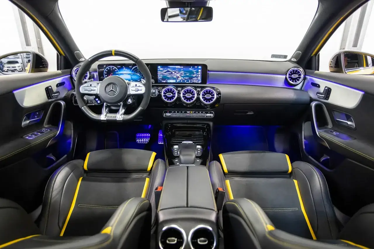 Wnętrze sportowego A45 AMG z czarną tapicerką i żółtymi akcentami, podświetlone niebieskim światłem.