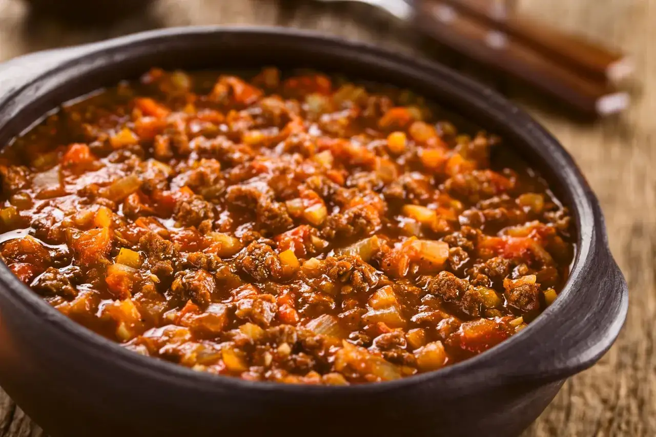 Un saporito ragù di cinghiale, ricco e denso, servito in una ciotola di terracotta su un tavolo di legno rustico.