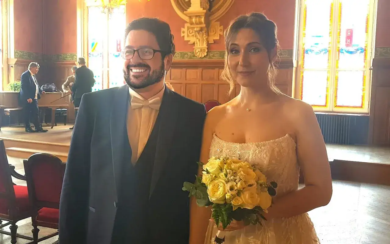 Un couple rayonnant c&eacute;l&egrave;bre son mariage avec un &eacute;tranger. La mari&eacute;e tient un bouquet de roses jaunes, le mari&eacute; porte un costume &eacute;l&eacute;gant.