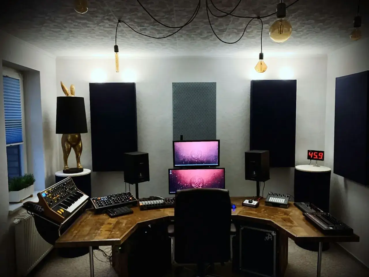 Studio d'enregistrement avec bureau en bois, claviers, &eacute;crans, enceintes et une lampe originale. La **stem d&eacute;finition** est ici la s&eacute;paration des pistes audio pour un mixage pr&eacute;cis.