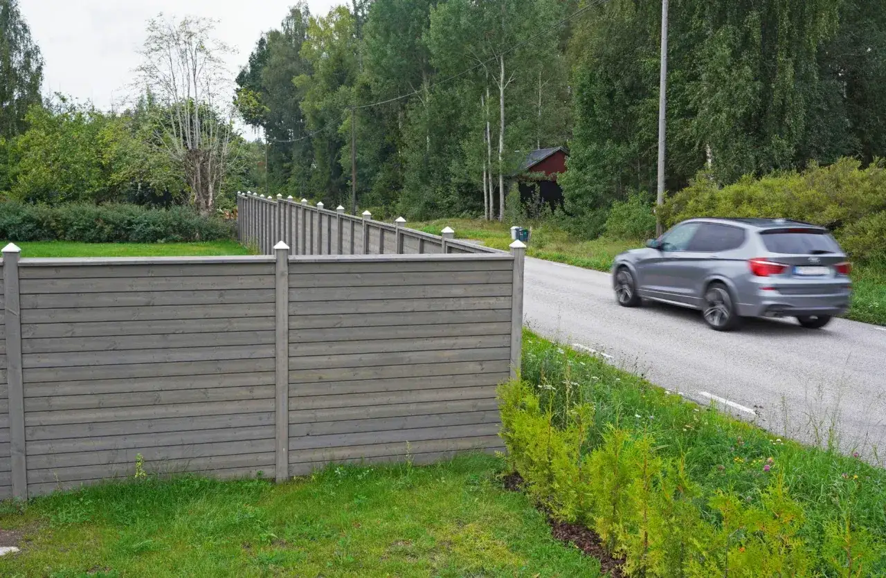 Grått bullerplank av trä längs en väg. En bil kör förbi. Perfekt för att bygga bullerplank.