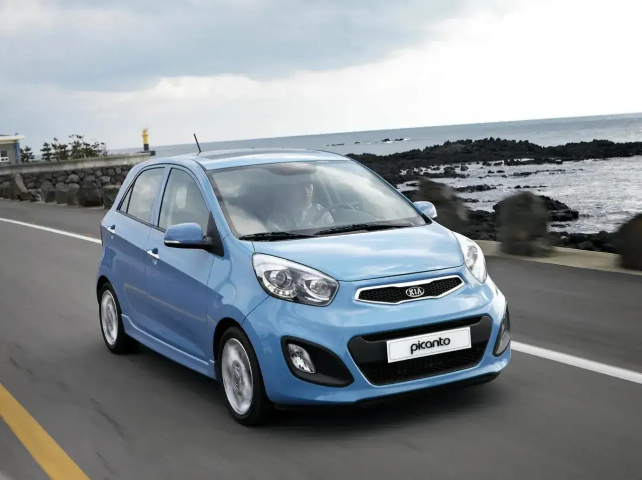 La Kia Picanto blu sfreccia lungo una strada costiera. Nonostante i suoi piccoli difetti, è un'auto agile e divertente da guidare.