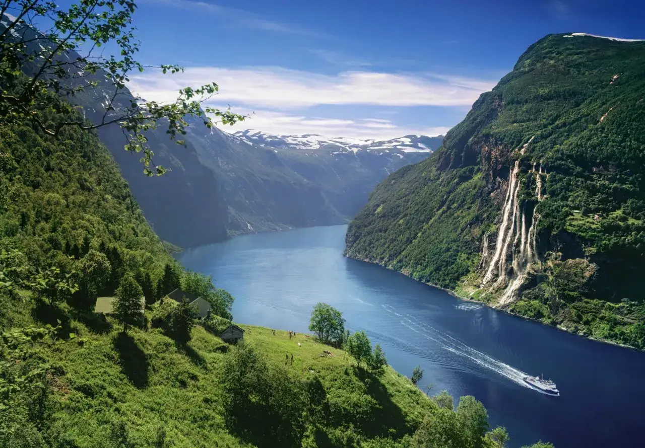 En b&aring;t f&auml;rdas p&aring; en djupbl&aring; fjord omgiven av gr&ouml;na berg med vattenfall. En idyllisk plats f&ouml;r of&ouml;rgl&ouml;mliga upplevelser i Norge.