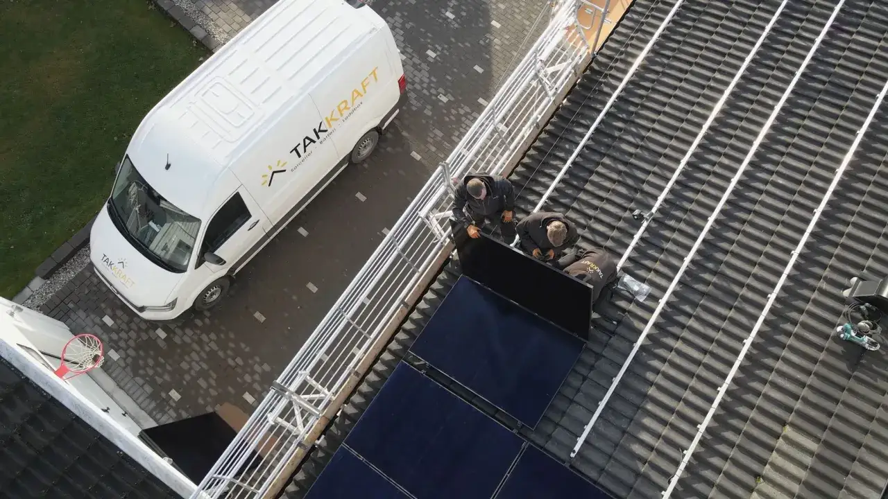 Tv&aring; mont&ouml;rer fr&aring;n **Takkraft AB** installerar solpaneler p&aring; ett tak. En vit servicebil med Takkraft AB:s logotyp st&aring;r parkerad bredvid.