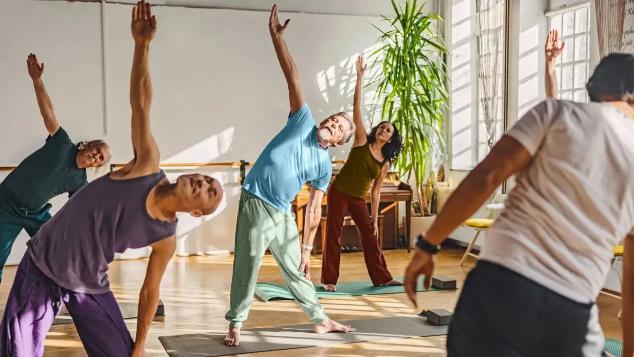 Senioren üben Yoga, eine gute Möglichkeit, welchen Sport bei COPD man machen kann. Sie dehnen sich in einem hellen Raum.