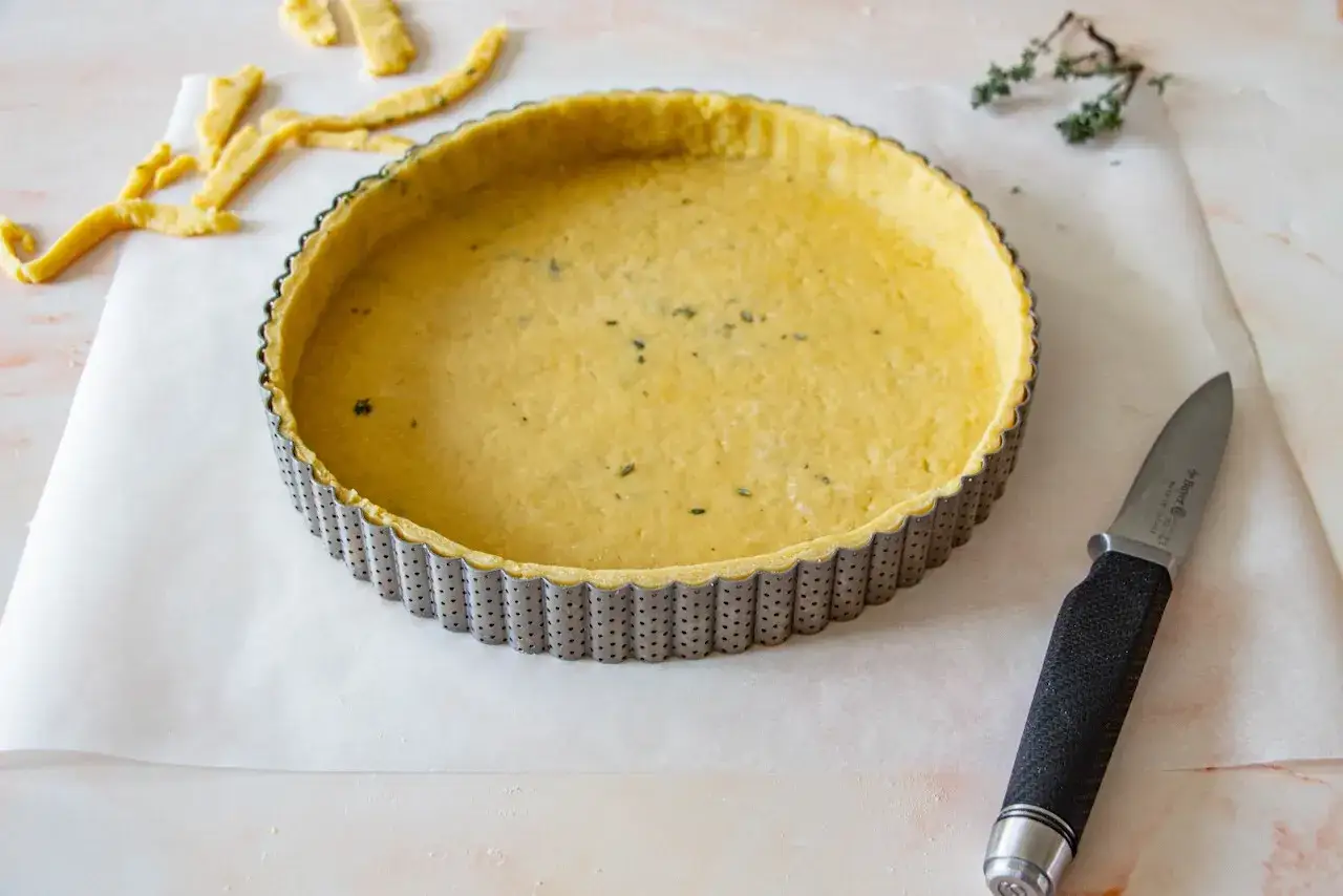 P&acirc;te bris&eacute;e pr&ecirc;te &agrave; &ecirc;tre cuite dans une casserole &agrave; tarte. Des chutes de p&acirc;te et un couteau sont &agrave; proximit&eacute;.
