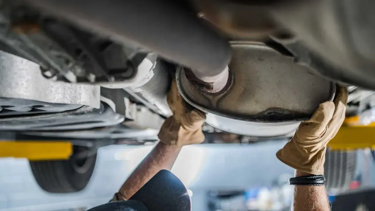 Mechanic's gloved hands work on a car's exhaust system, a key part of any tune up.