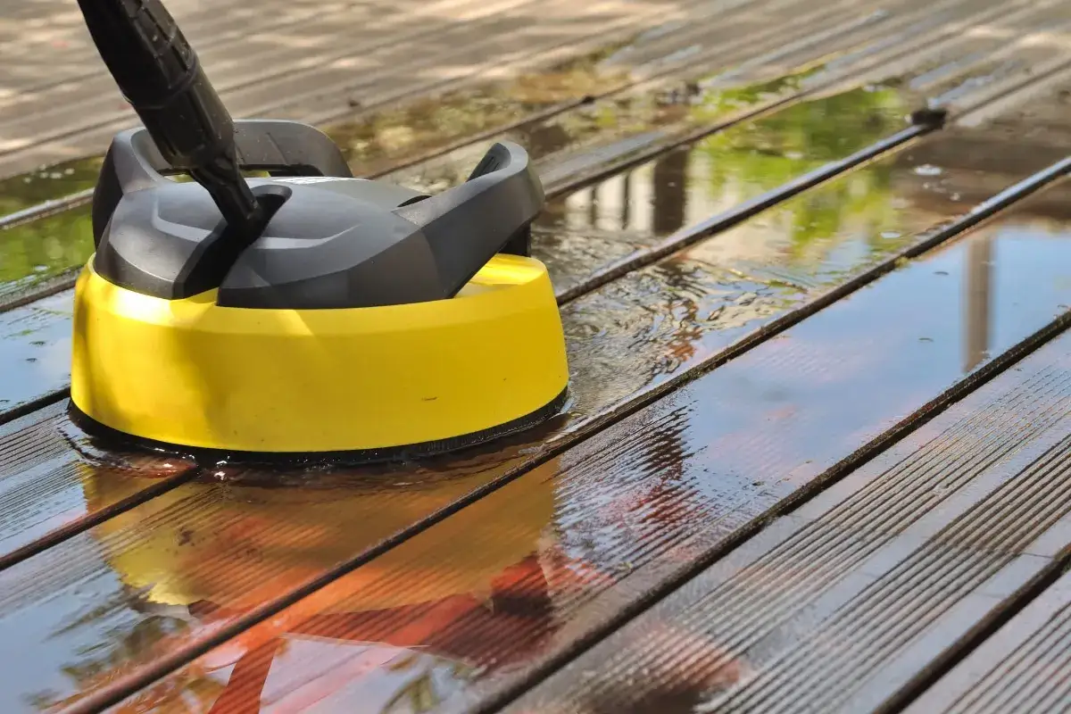 Nettoyage d'une terrasse en bois avec un appareil jaune et noir. L'eau refl&egrave;te le ciel et la v&eacute;g&eacute;tation. Un entretien de terrasse bois efficace.