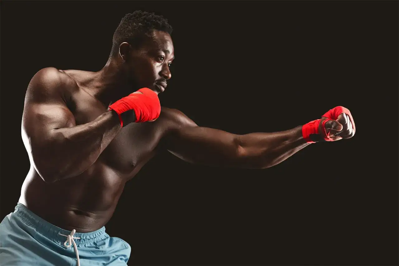 En muskul&ouml;s man med r&ouml;da boxningslindor tr&auml;nar slag. Han visar vad som kr&auml;vs f&ouml;r att f&ouml;rst&aring; vad betyder MMA.