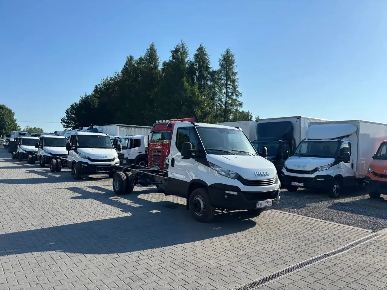 Rząd białych Iveco 70c18, gotowych do zabudowy, stoi na placu parkingowym.