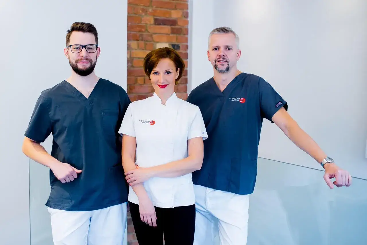 Trzech dentystów w fartuchach medycznych, dwóch mężczyzn i kobieta, pozuje do zdjęcia.