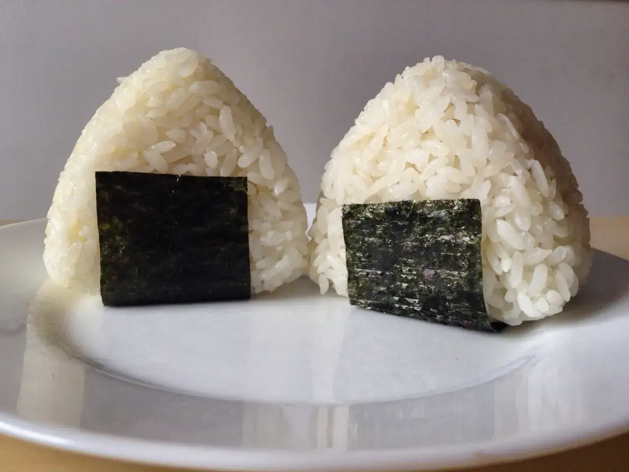 Dwa ryżowe onigiri z paskami nori na białym talerzu. Idealne na szybki lunch, prosty onigiri przepis.