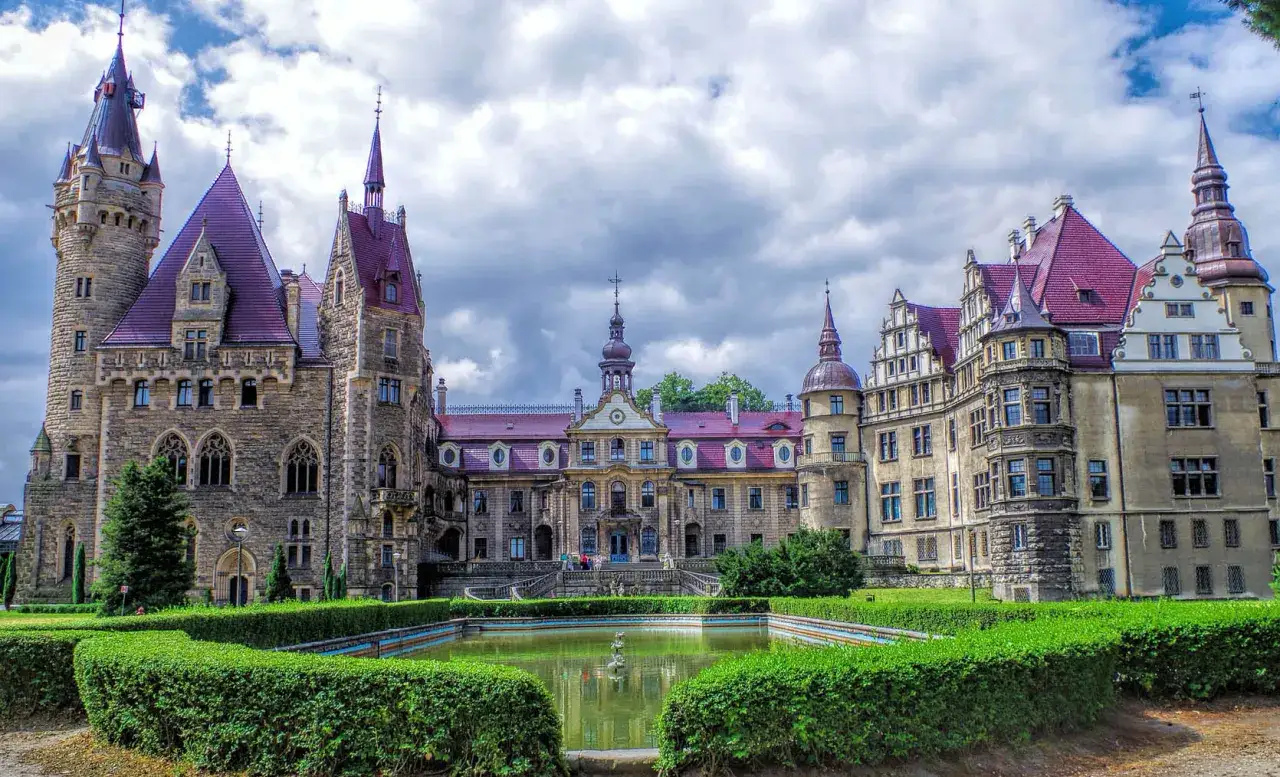 Zamek Moszna, co to za cudowna budowla! Majestatyczny zamek z wieżami i czerwonymi dachami, otoczony zielenią i stawem.
