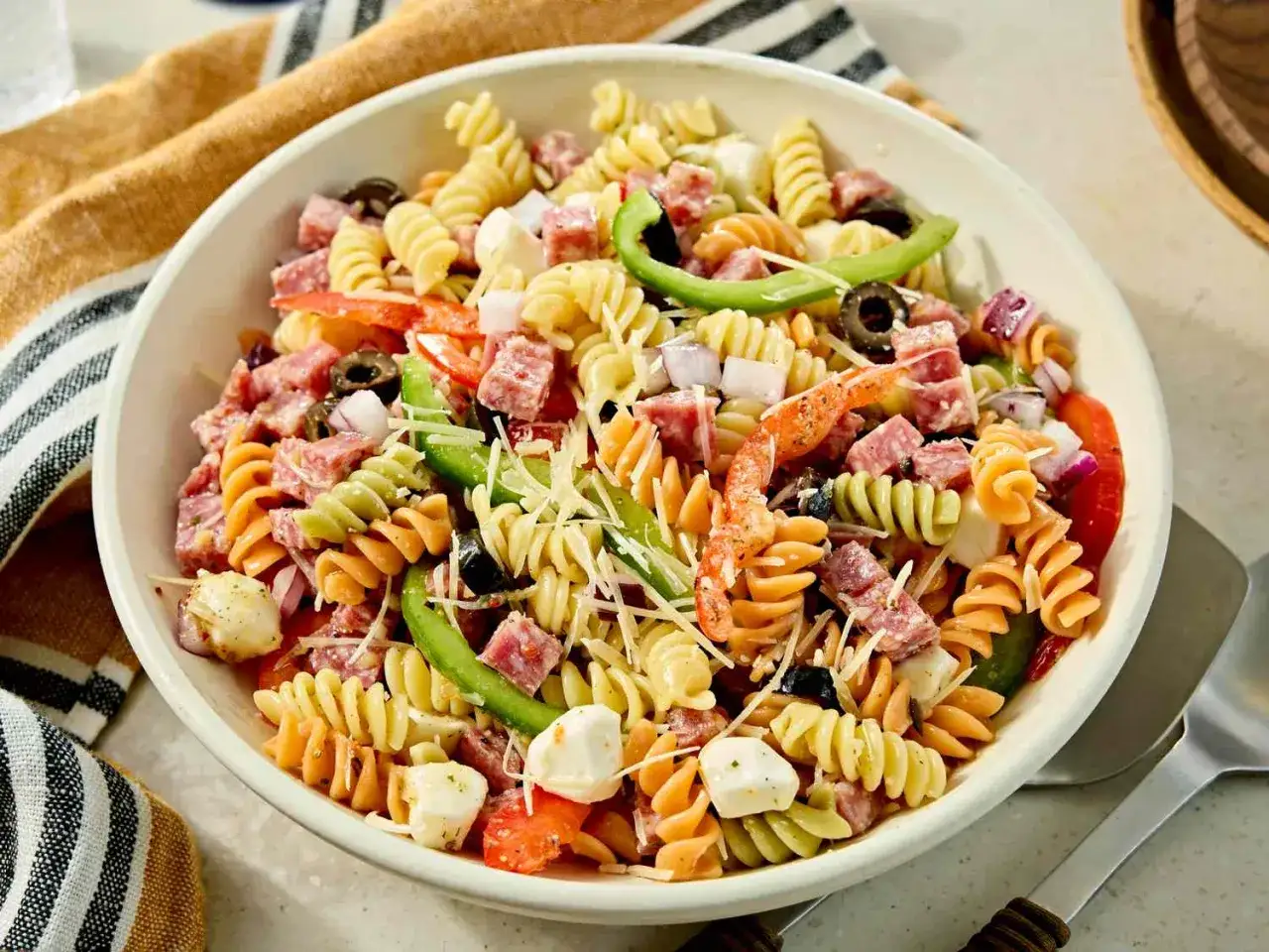 Ensalada de pasta colorida con salami, queso mozzarella, aceitunas, pimientos y cebolla roja, ba&ntilde;ada en una deliciosa salsa para ensalada de pasta.