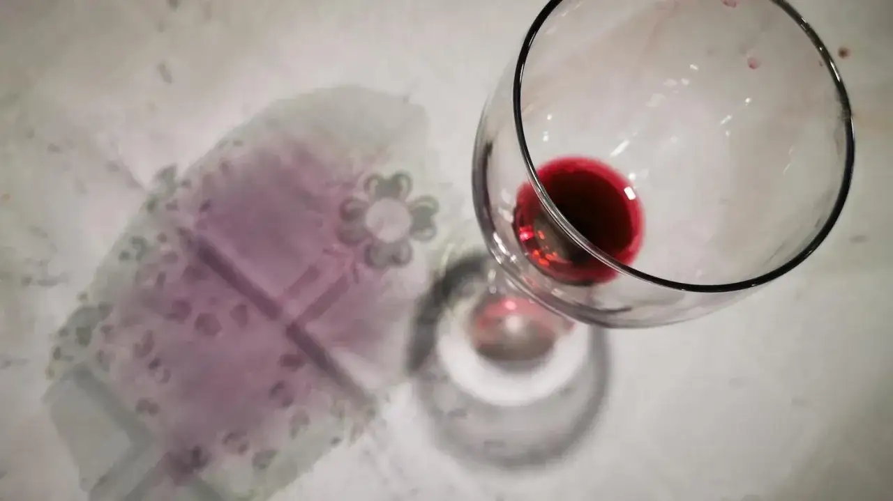 Un bicchiere di vino rosso rovesciato su una tovaglia con un disegno floreale. Le macchie di vino rosso vanno via, lasciando solo un ricordo.