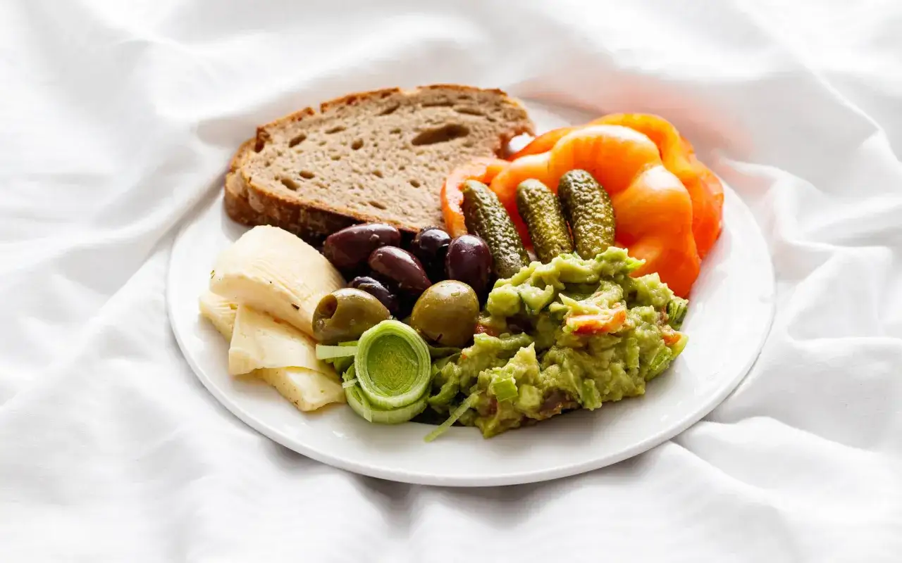 Talerz z serem, oliwkami, ogórkami, guacamole, pieczywem i pomidorem. Idealna przekąska dla wegetarianina.