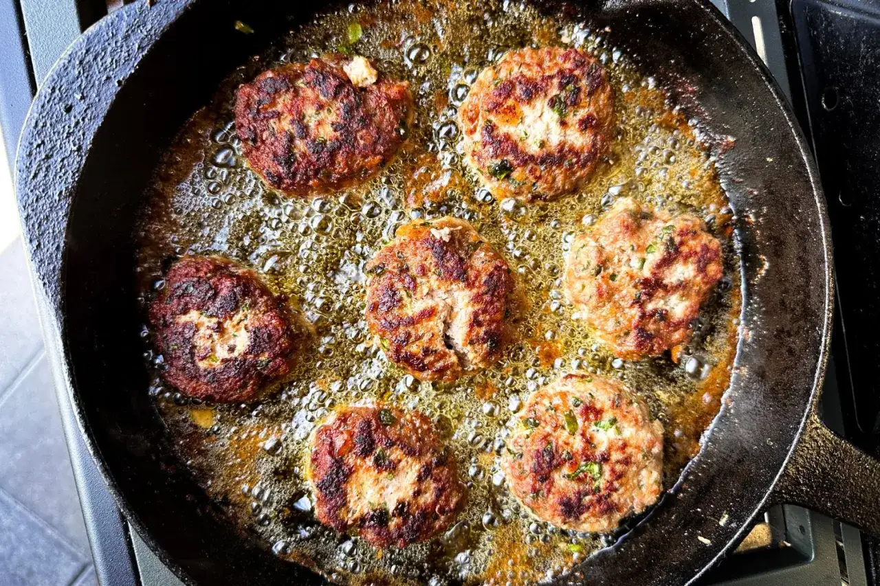 Sechs goldbraune Buletten brutzeln in hei&szlig;em &Ouml;l in einer Gusseisenpfanne. Ein k&ouml;stliches Buletten Rezept in Aktion.