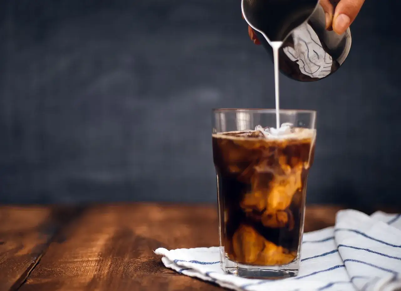 Milch wird in ein Glas mit Eis und Kaffee gegossen. Ein erfrischender Cold Brew Eiskaffee entsteht.