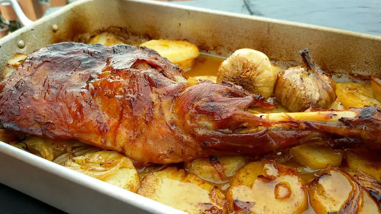 Paletilla de cordero al horno, dorada y jugosa, acompañada de patatas y ajos asados en su jugo.