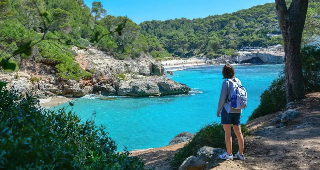 Una persona con mochila admira la cala Macarella, un lugar ideal que ver en Menorca en 3 días.