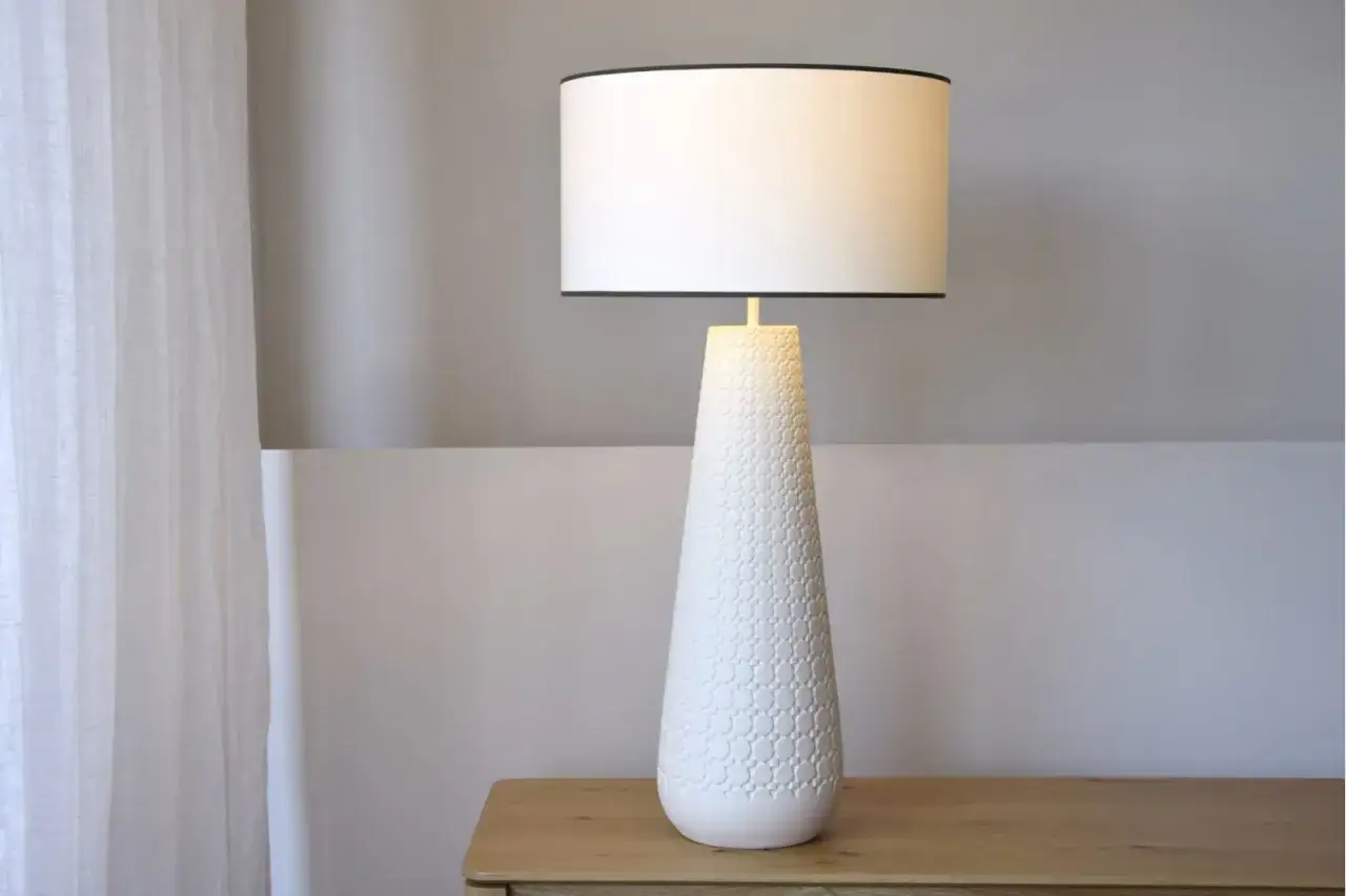 Elegantes l&aacute;mparas de mesa blancas con base texturizada y pantalla cil&iacute;ndrica, iluminando un rinc&oacute;n acogedor junto a una cortina vaporosa.