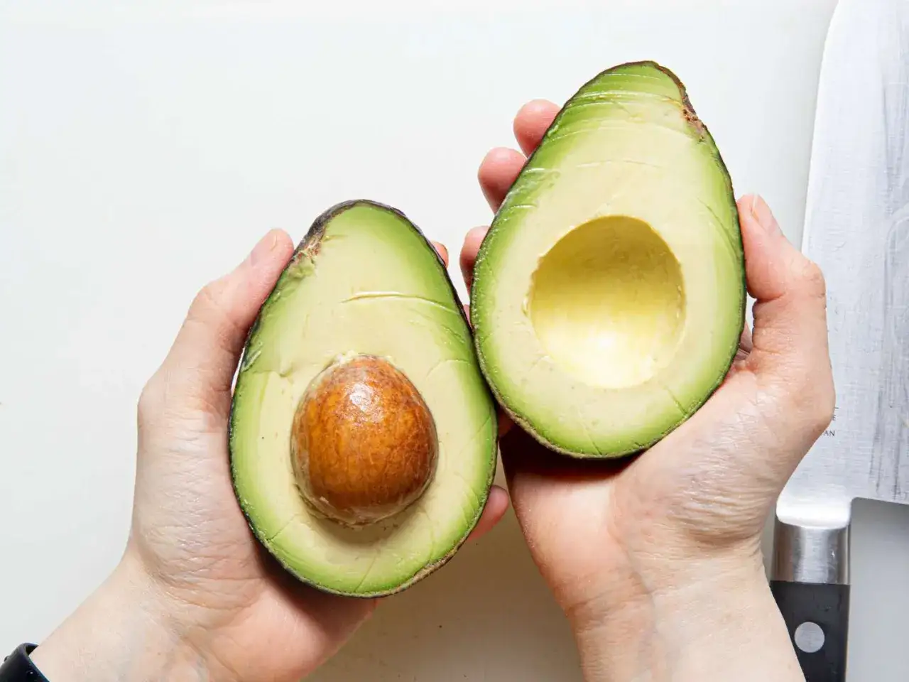 Dwie poł&oacute;wki awokado hass w dłoniach. Jedna z pestką, druga pusta, gotowa do przygotowania guacamole.