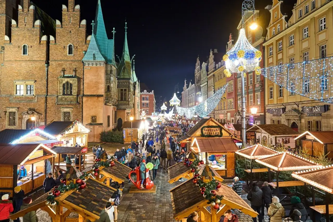 Tłoczny jarmark we Wrocławiu nocą, pełen straganów, światełek i ludzi.