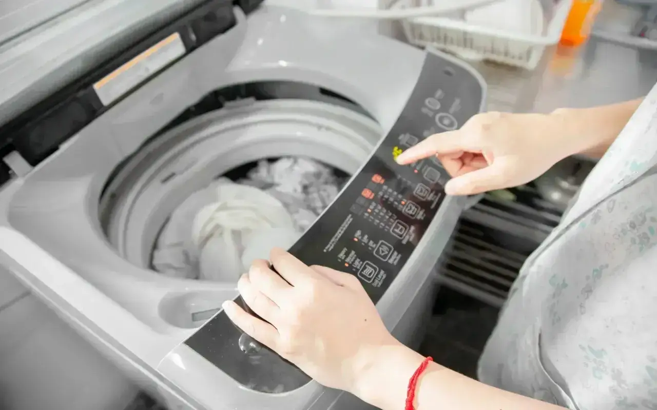 Mano che imposta la lavatrice per lavare pile, selezionando la temperatura corretta.